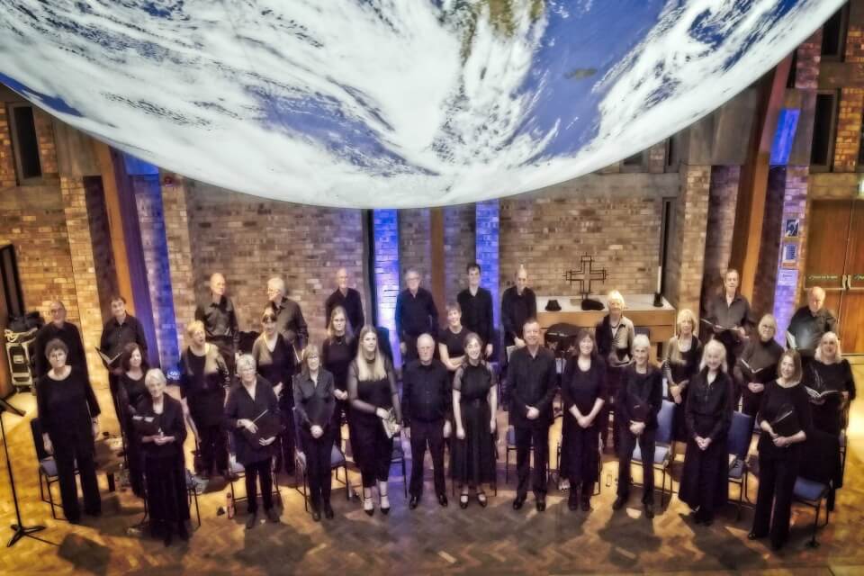 Keele Bach Choir Members congregate below a large suspended globe in Keel Chapel.